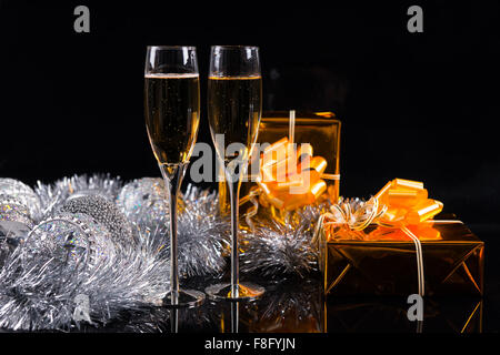 Two stemmed glasses full of champagne, Christmas silver tinsel and two gift boxes wrapped in golden shiny paper on a table with Stock Photo