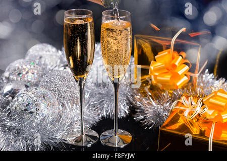 Sparkling champagne for Christmas in two elegant flutes with silver decorations and golden gifts in a festive background Stock Photo