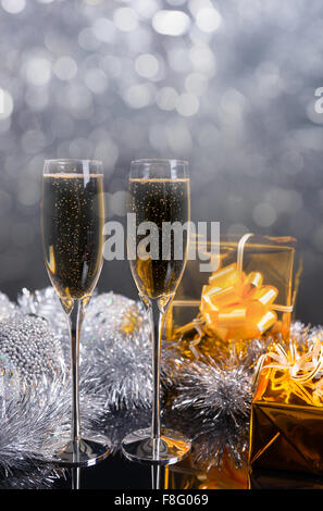 Festive Christmas Still Life with Copy Space - Pair of Glasses Filled with Sparkling Champagne, Gifts Wrapped in Gold Paper and Silver Decorations on Table. Stock Photo