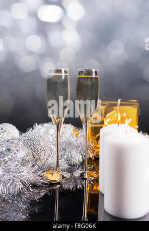 Festive Christmas Still Life with Glittering Background - Pair of Glasses Filled with Sparkling Champagne on Table with Gifts, Silver Decorations and Lit White Pillar Candles. Stock Photo