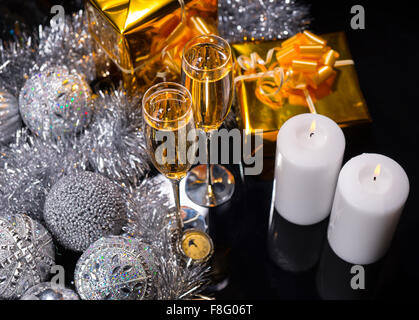 High Angle Festive Christmas Still Life - Pair of Glasses Filled with Sparkling Champagne on Table with Gifts, Silver Decorations and Lit White Pillar Candles on Black Surface. Stock Photo