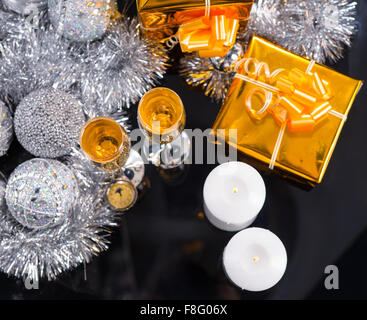 High Angle Festive Christmas Still Life - Pocket Watch, Glasses of Champagne, Two Lit Candles and Gifts Wrapped in Gold Paper with Silver Tinsel Garland and Decorative Balls. Stock Photo