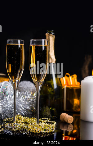 Festive Christmas Still Life - Two Glasses of Sparkling Champagne with String of Gold Beads, Bottle of Champagne and Decorations in front of Black Background. Stock Photo