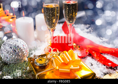 Festive Still Life with Copy Space - Pocket Watch on top of Gold Wrapped Gift in Still Life with Champagne Glasses, Lit Candles and Glittering Christmas Decorations. Stock Photo