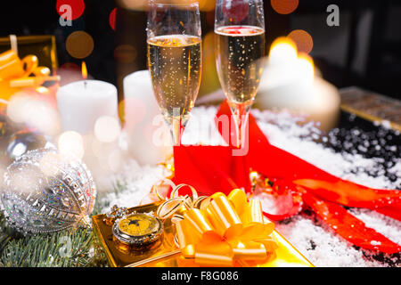 Festive Still Life - Pocket Watch on top of Gold Wrapped Gift in Still Life with Champagne Glasses, Lit Candles and Glittering Christmas Decorations. Stock Photo