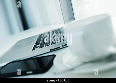 Laptop Computer on a Desk Shallow Field Closeup. Cup of Coffee in a White Cup. Online Remote Home Workstation. Stock Photo