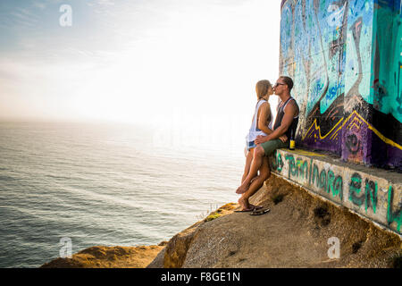 Caucasian couple kissing at mural on cliff Stock Photo