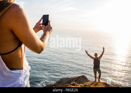 Caucasian man photographing girlfriend on cliff Stock Photo
