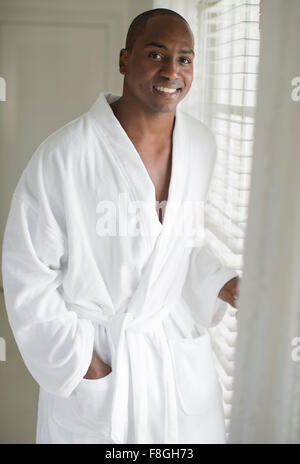 Black man in bathrobe standing at window Stock Photo