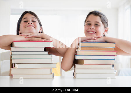 Caucasian twin sisters resting on stacks of books Stock Photo