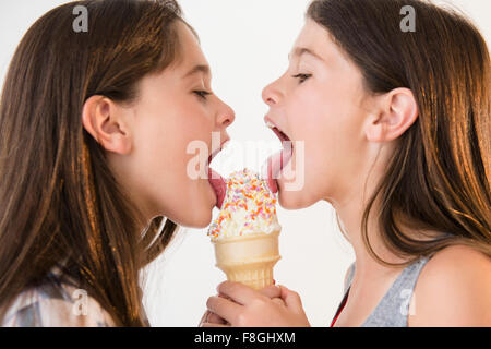 Caucasian twin sisters sharing ice cream cone Stock Photo