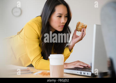 Chinese businesswoman using laptop and eating Stock Photo