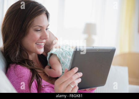 Mother using digital tablet and holding baby daughter Stock Photo