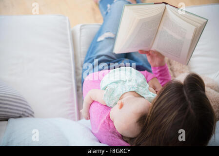Mother reading book and holding baby daughter Stock Photo