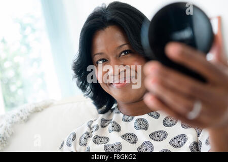 Black woman admiring herself in compact mirror Stock Photo