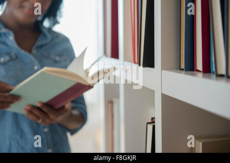 Black woman reading book at bookcase Stock Photo