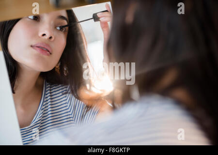 Hispanic woman applying mascara in mirror Stock Photo