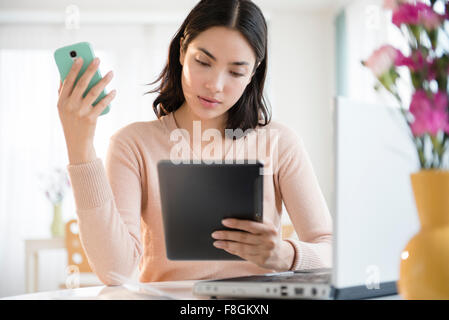 Hispanic woman using cell phone and digital tablet Stock Photo