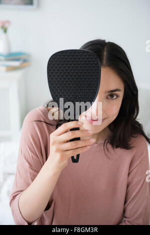 Hispanic woman peeking out from behind hand mirror Stock Photo