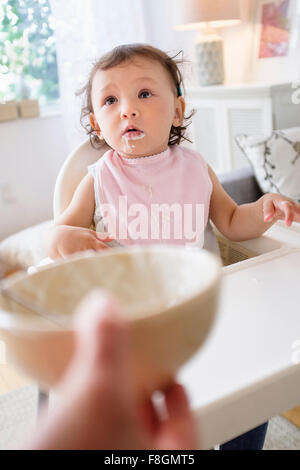 Mother feeding baby daughter in high chair