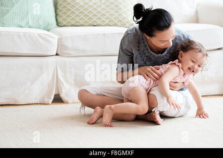 Mother and baby daughter playing in living room Stock Photo