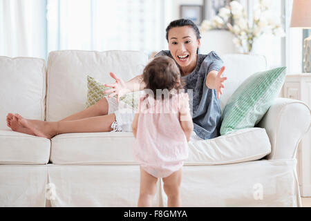 Mother reaching for baby daughter on sofa Stock Photo