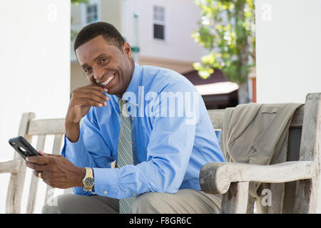 Black businessman using cell phone on bench Stock Photo