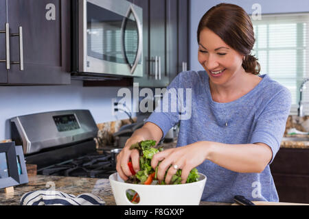 Mixed race woman tossing salad in kitchen Stock Photo