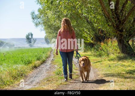 Caucasian woman walking dog on dirt path Stock Photo