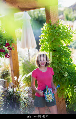 Mixed race woman holding watering can in garden Stock Photo