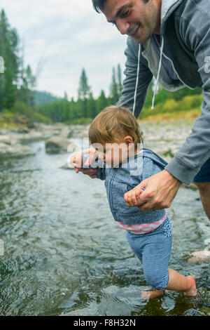 Father helping daughter walk in river Stock Photo