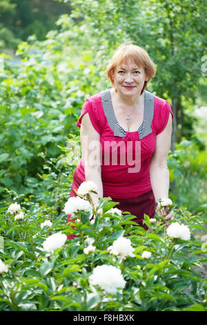 Happy mature woman in yard gardening with peony plant Stock Photo