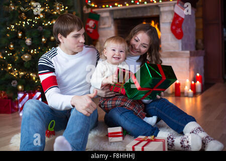 Happy family - father, mother and little son sitting with gifts near Christmas tree and fireplace