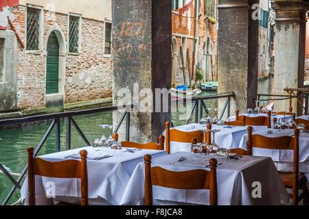 Wooden tables on narrow street among typical colorful houses and small bridge in Venice, Italy. Stock Photo