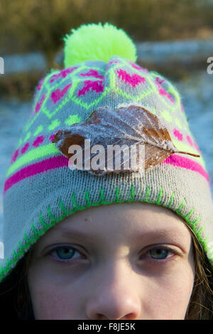 Young girl with bobble hat on with a frosty leaf on it, looking at the camera Stock Photo