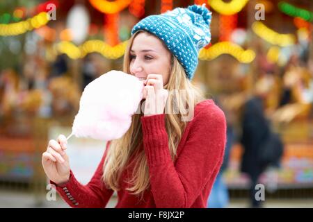 Young woman eating candy floss at funfair, outdoors Stock Photo