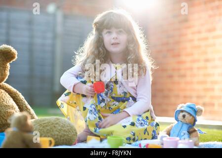 Girl having teddy bear picnic in garden holding toy teacup Stock Photo