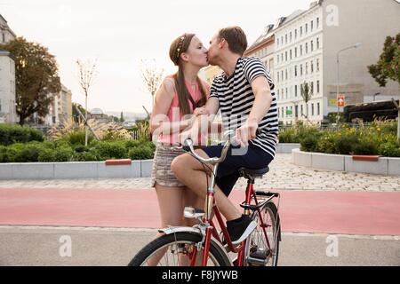 Young man sitting on bicycle kissing young woman Stock Photo