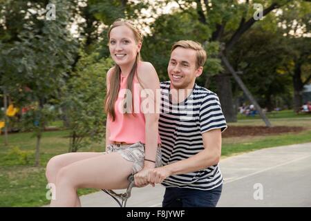 Young man riding bicycle with young woman sitting on handlebars smiling Stock Photo