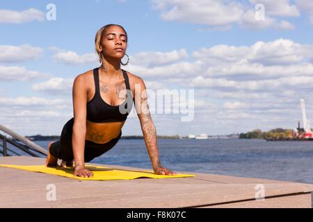 Young woman sitting cross legged by water in yoga position, eyes closed,  Philadelphia, Pennsylvania, USA stock photo
