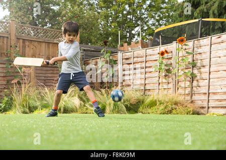 Boy playing cricket in garden, ball in mid air Stock Photo