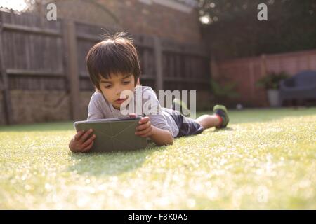 Boy in garden lying on front on grass looking down using digital tablet Stock Photo