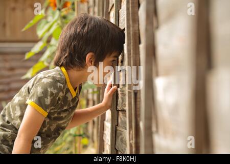 Waist up side view of boy peeking through wooden fence Stock Photo