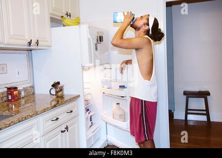Young man standing next to open fridge, drinking milk from carton Stock Photo