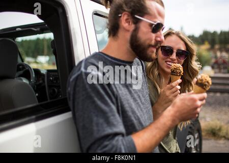 Young couple leaning against jeep eating ice cream cones Stock Photo