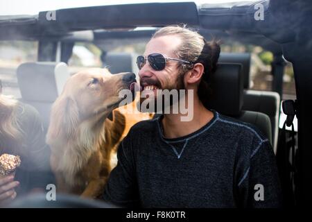 Dog licking young mans bearded face in jeep Stock Photo