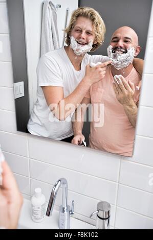 Bathroom mirror image of male couple having fun shaving Stock Photo