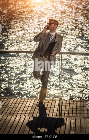 High angle view of young businessman talking on smartphone on sunlit waterfront Stock Photo