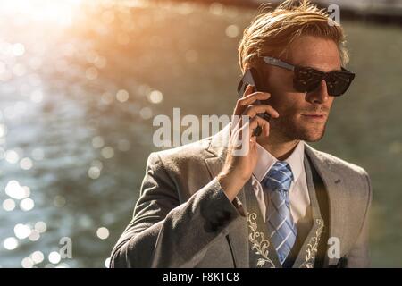 Young businessman wearing sunglasses talking on smartphone on waterfront Stock Photo