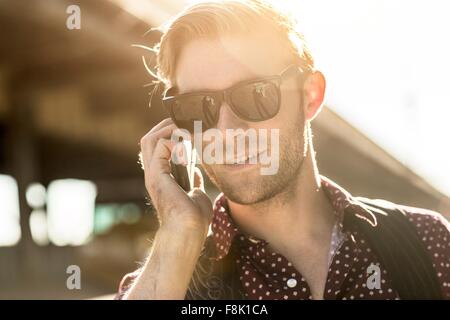 Young businessman wearing sunglasses talking on smartphone on city street Stock Photo